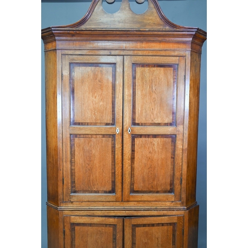 1028 - A Georgian oak corner cupboard, in two parts, the upper with broken swan-neck pediment over a pair o... 