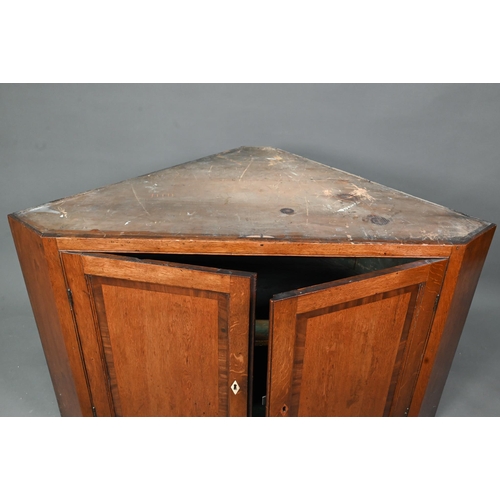 1028 - A Georgian oak corner cupboard, in two parts, the upper with broken swan-neck pediment over a pair o... 