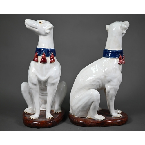 639 - A pair of 20th century glazed terracotta heraldic seated talbots with tasselled collars, on oval bas... 