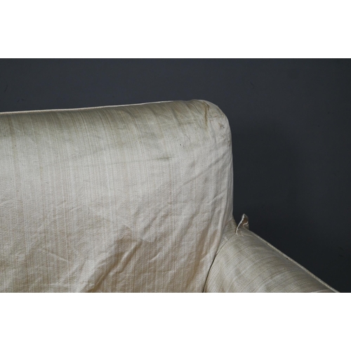 963 - A traditional two-seat sofa with gold silk loose covers over patterned undercloth, raised on hip car... 