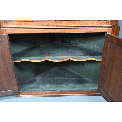 1028 - A Georgian oak corner cupboard, in two parts, the upper with broken swan-neck pediment over a pair o... 