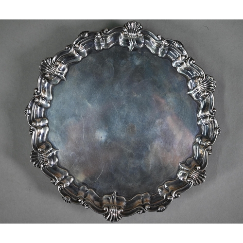 173 - An Edwardian circular silver card salver in the Georgian manner, with shell and scroll moulded borde... 