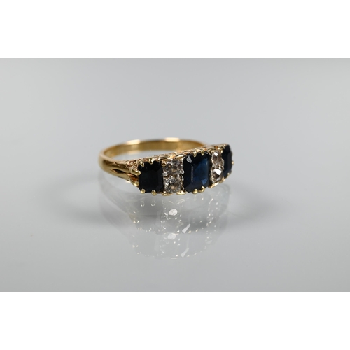 236 - An 18ct yellow gold ring set with three graduated rectangular dark blue sapphires with diamonds betw... 