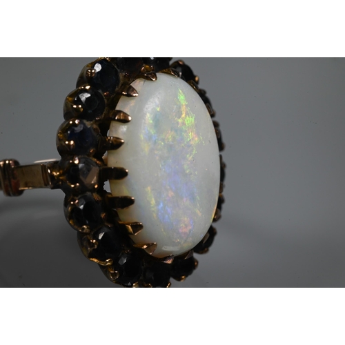 255 - An opal dress ring, the white oval opal surrounded by dark blue stones, yellow metal set, size Q, 2.... 