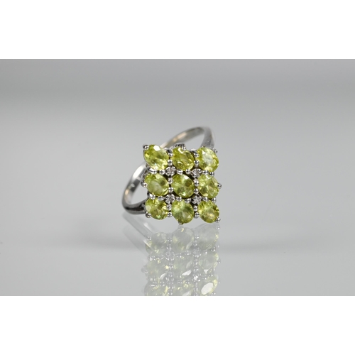 262 - A cluster ring comprising nine oval peridots, claw set with four diamonds between, white metal set s... 