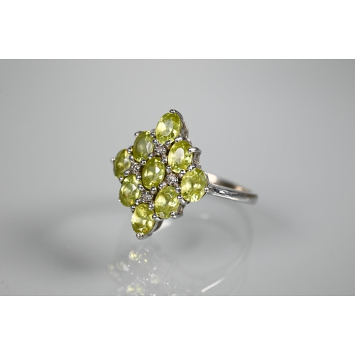 262 - A cluster ring comprising nine oval peridots, claw set with four diamonds between, white metal set s... 