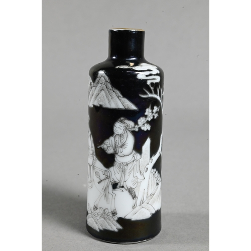 A 19th century Chinese black ground en-grisaille porcelain snuff bottle of high shouldered cylindrical from, with gilded rim and painted with a narrative scene (Romance of the three Kingdoms) with Huang Chengyan riding his donkey and his attendant holding a branch of prunus in a mountainous landscape setting, missing stopper and spoon, the base with four-character Ming seal mark but Qing dynasty, 8 cm high