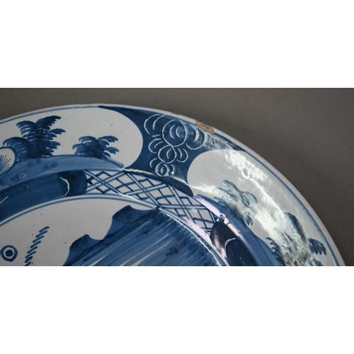 610 - A Delft blue and white plate, painted with chinoiserie coastal landscape within foliate reserves rim... 