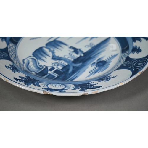 610 - A Delft blue and white plate, painted with chinoiserie coastal landscape within foliate reserves rim... 