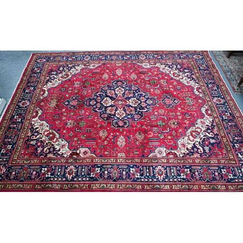 A Persian Heriz carpet, the red ground with stylised floral design centred by a blue medallion, 385 cm x 295 cm