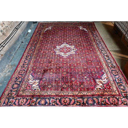 387 - An old Persian Hamadan carpet, the red ground with repeating stylised floral design centred by a med... 