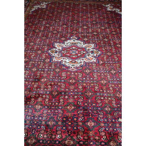 387 - An old Persian Hamadan carpet, the red ground with repeating stylised floral design centred by a med... 