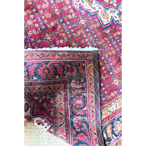 387 - An old Persian Hamadan carpet, the red ground with repeating stylised floral design centred by a med... 