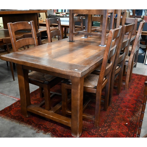 A rustic oak dining table with cleated rectangular top on square supports united by stretchers, 220 cm wide x 90 cm deep x 76 cm high to/w ten ladderback chairs comprising six standard and four carvers, with woven rush seats