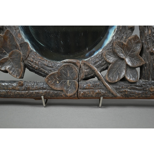 140 - A late 19th century Black Forest wall mirror, the oval bevelled edge mirror set within a frame carve... 