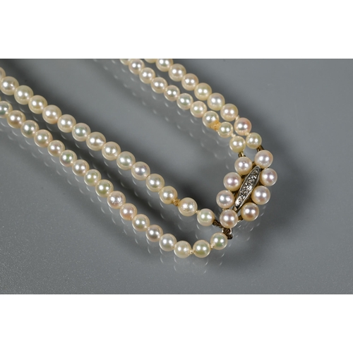 216 - A pearl necklace comprising two rows of graduated cultured pearls on oval pearl and diamond set snap... 