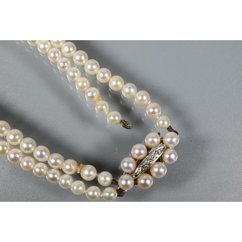 216 - A pearl necklace comprising two rows of graduated cultured pearls on oval pearl and diamond set snap... 