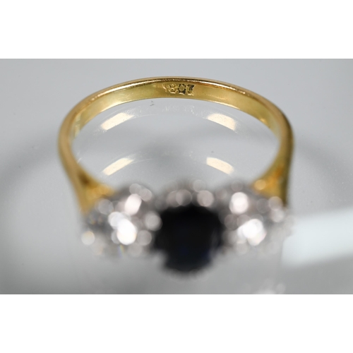 255 - A three-stone sapphire and diamond ring, the central oval blue sapphire with a circular diamond to e... 