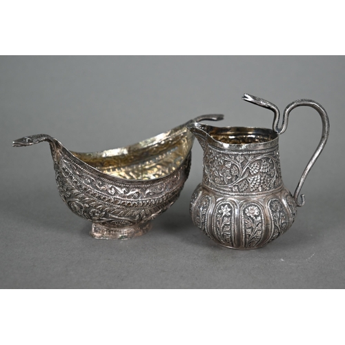 49 - An Indian low-grade silver small cream and sugar pair with cobras' heads handles and foliate chased ... 