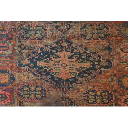 821 - An antique Caucasian Sumak / Soumak carpet, the brown-red ground with geometric guls within wide bor... 