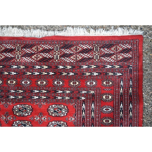 834 - A contemporary Turkoman red ground carpet, the repeating gul design within wide borders, 364 cm x 28... 