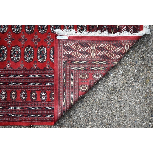 834 - A contemporary Turkoman red ground carpet, the repeating gul design within wide borders, 364 cm x 28... 