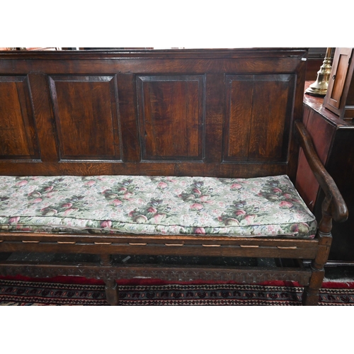 934 - A Georgian oak four panel back settle, the shaped and swept arms over a rope seat (with later cushio... 