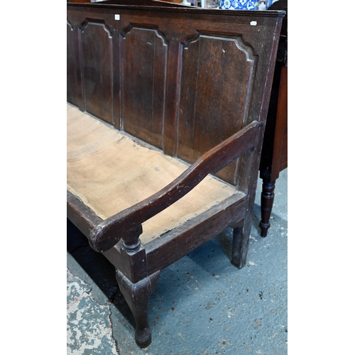 969 - An 18th century oak settle, the shaped four panel back over shaped arms and a sacking covered seat, ... 