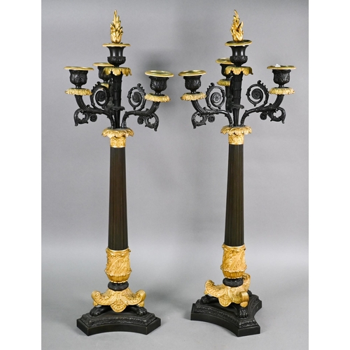 985 - A pair of dark bronzed and gilt metal five candle column candelabra, in the Empire style, raised on ... 