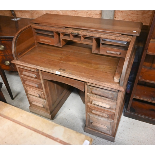 241 - A compact light oak roll top desk, with nine drawers, raised on twin plinth bases to castors - by re... 