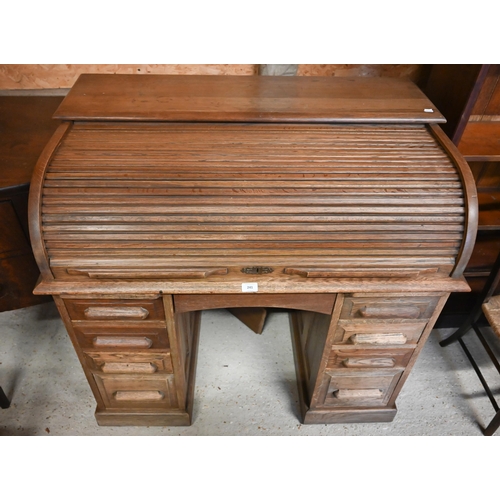 241 - A compact light oak roll top desk, with nine drawers, raised on twin plinth bases to castors - by re... 