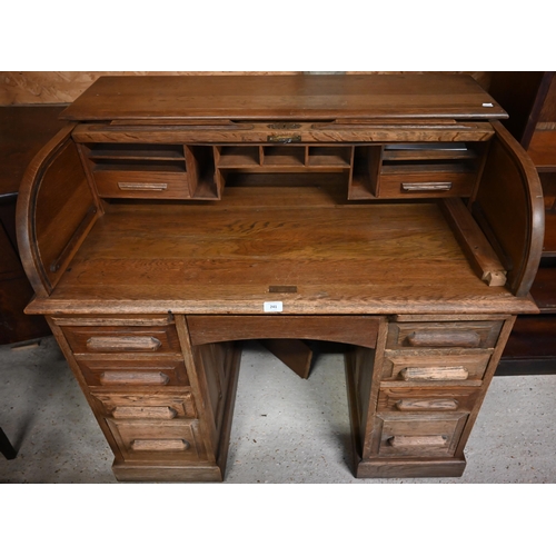 241 - A compact light oak roll top desk, with nine drawers, raised on twin plinth bases to castors - by re... 