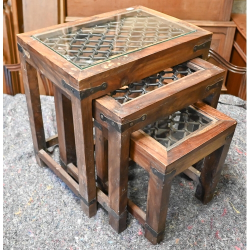 105 - A trio of Indian hardwood nest of tables with iron grilled top under glass, the largest 44.5 x 30 x ... 