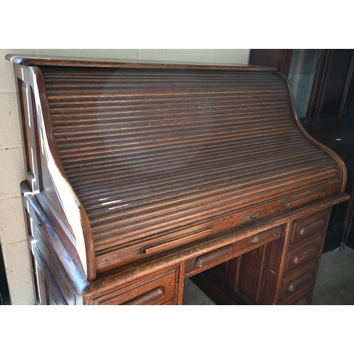 73 - An early 20th century oak roll-top desk, the sliding tambour panel enclosing a fitted interior over ... 