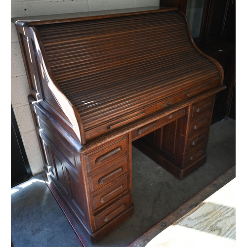 73 - An early 20th century oak roll-top desk, the sliding tambour panel enclosing a fitted interior over ... 