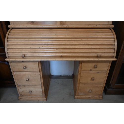 84 - A pine roll-top desk bookcase, pair of glazed doors over sliding tambour panel enclosing fitted inte... 