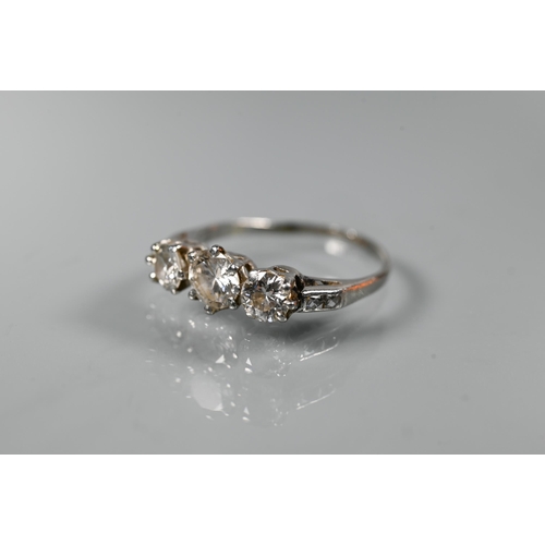 225 - A diamond ring, the three graduated diamonds claw set with diamond set shoulders, white metal set st... 