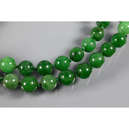 279 - WITHDRAWN A row of uniform round jade beads, varying hues of green, double knotted throughout, 60 cm... 