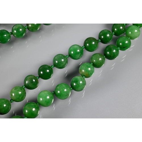 279 - WITHDRAWN A row of uniform round jade beads, varying hues of green, double knotted throughout, 60 cm... 