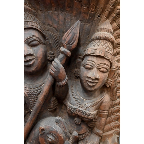 566 - An Indian high-relief carved hardwood panel depicting Karkikeya (Hindu God of War) and his two conso... 