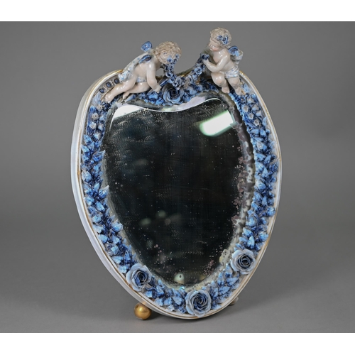 671 - An antique Sitzendorf porcelain heart-shaped mirror surmouted by two cherubs, on floral-encrusted fr... 