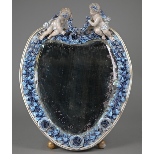 671 - An antique Sitzendorf porcelain heart-shaped mirror surmouted by two cherubs, on floral-encrusted fr... 