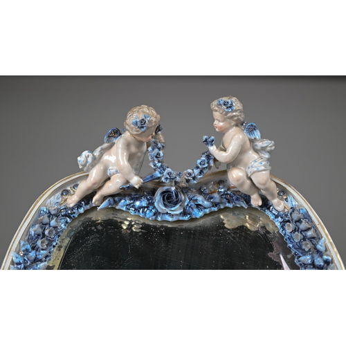 671 - An antique Sitzendorf porcelain heart-shaped mirror surmouted by two cherubs, on floral-encrusted fr... 