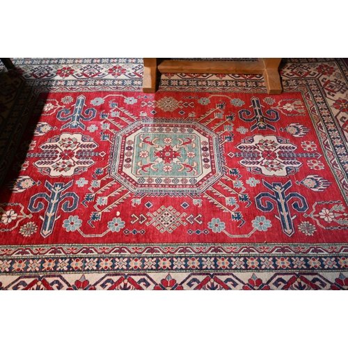 1227 - A contemporary Kazak carpet with pale red ground and stylized floral design within camel ground bord... 