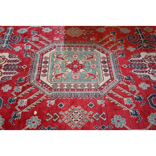 1227 - A contemporary Kazak carpet with pale red ground and stylized floral design within camel ground bord... 