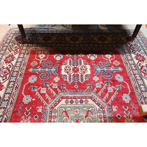 1227 - A contemporary Kazak carpet with pale red ground and stylized floral design within camel ground bord... 