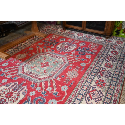 1227 - A contemporary Kazak carpet with pale red ground and stylized floral design within camel ground bord... 