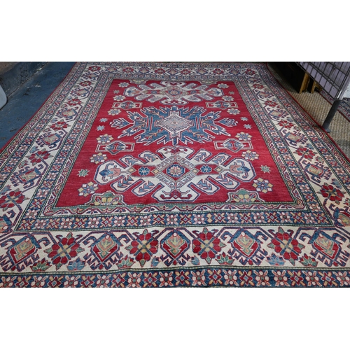 1228 - A contemporary Kazak carpet with pale red ground and stylized floral design within camel ground bord... 