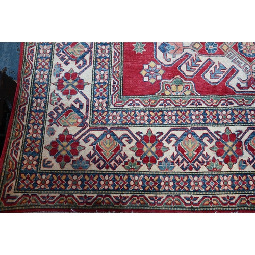 1228 - A contemporary Kazak carpet with pale red ground and stylized floral design within camel ground bord... 