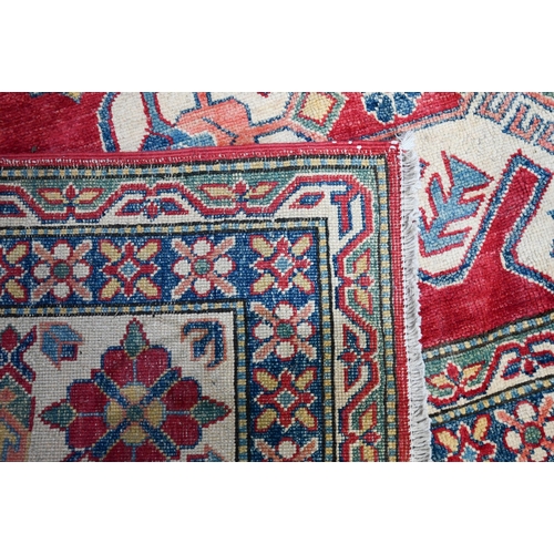 1228 - A contemporary Kazak carpet with pale red ground and stylized floral design within camel ground bord... 